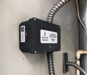A small box is mounted on a wall with cords running in and out.