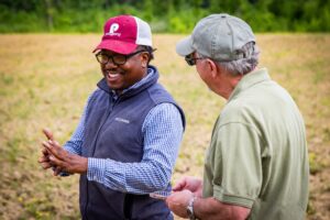 Two men stand in a field talking candidly. 