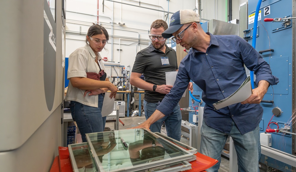 Three people with safety glasses stand in a lab setting looking at a glass product.