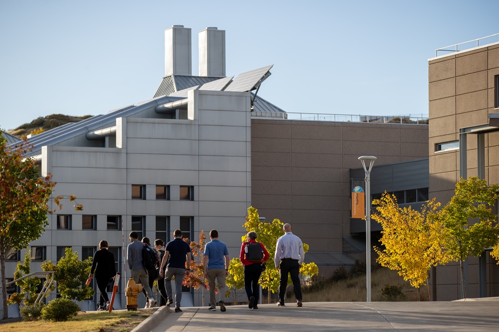 A group of people walk outside in front of a stairstep building.