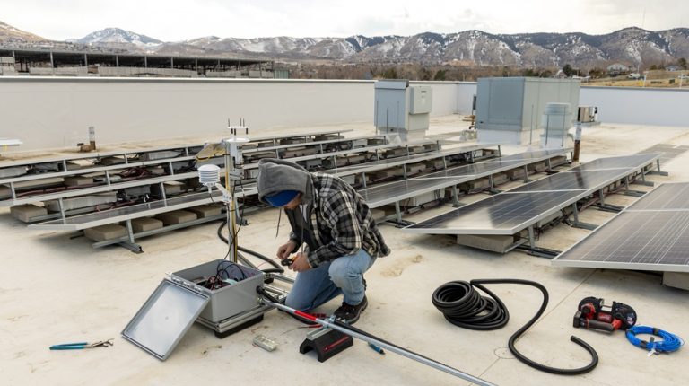 A person works on an electrical box on top of a building roof.