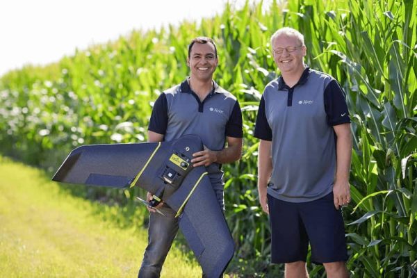 Two men pose with a drone in a cornfield.