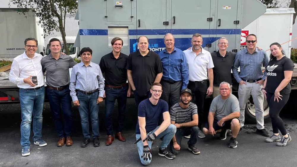 Blue Frontier Team pose for a picture in front of an air conditioning system on a flatbed trailer.