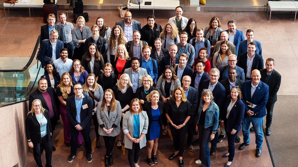 A diverse group of 50 people pose and smile, looking up at the camera.