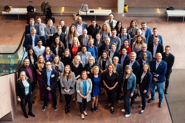 A diverse group of 50 people pose and smile, looking up at the camera.