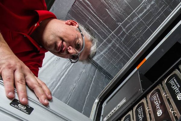 A man stands over a machine and adds a blade to the rack.