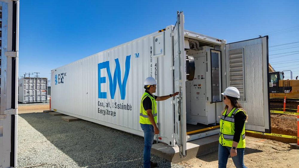 Two people in hard hats and safety vests open a large storage container reading "ESS EW."