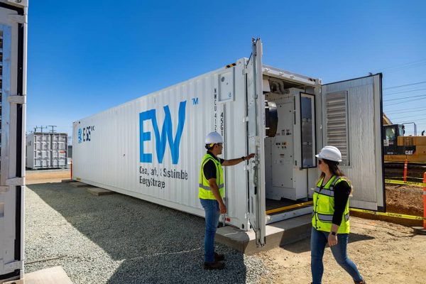 Two people in hard hats and safety vests open a large storage container reading "ESS EW."