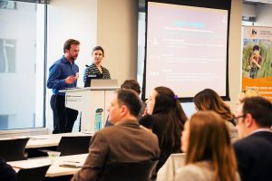 Two people present slides to a full meeting room.