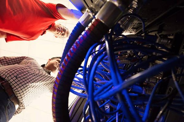 Engineers work on the Liquid Submerged Server's thick coolant hoses at the ESIF’s high performance computing data center.