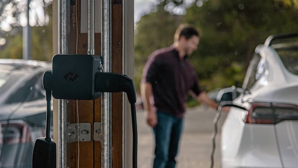 A man charges his car in front of NeoCharge technology.