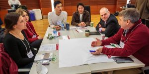 A group of six people sit around a table talking candidly.