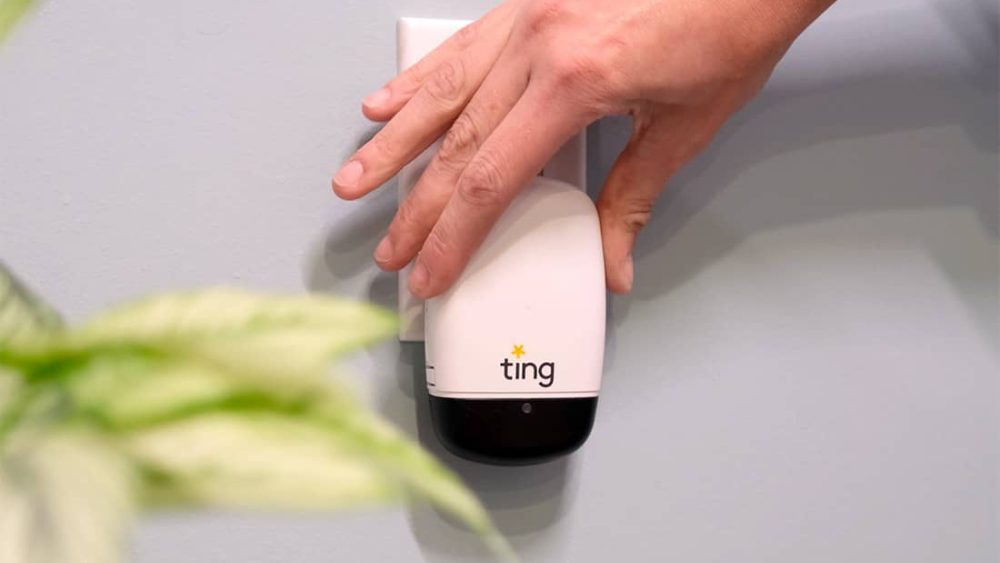 Small sensor with the name Ting on it plugged into a wall outlet. A hand is just above it after plugging it in.