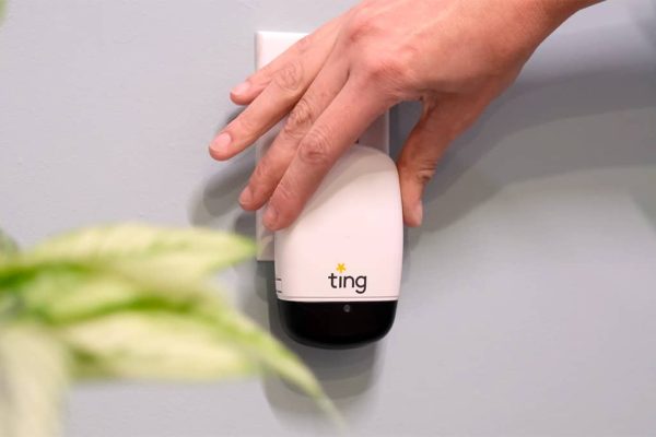 Small sensor with the name Ting on it plugged into a wall outlet. A hand is just above it after plugging it in.