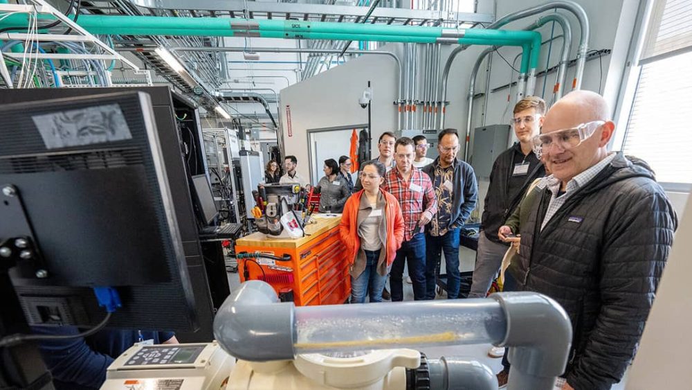 A group of people stand in a lab looking at a machine. Photo courtesy of NREL