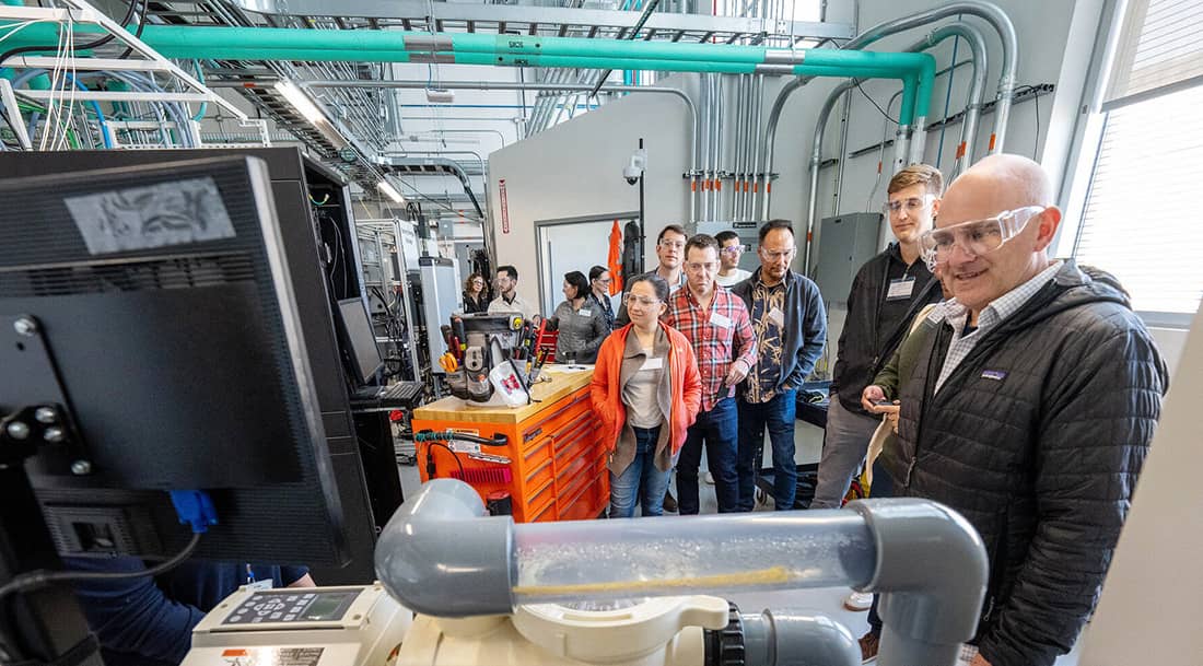 A group of people stand in a lab looking at a machine. Photo courtesy of NREL