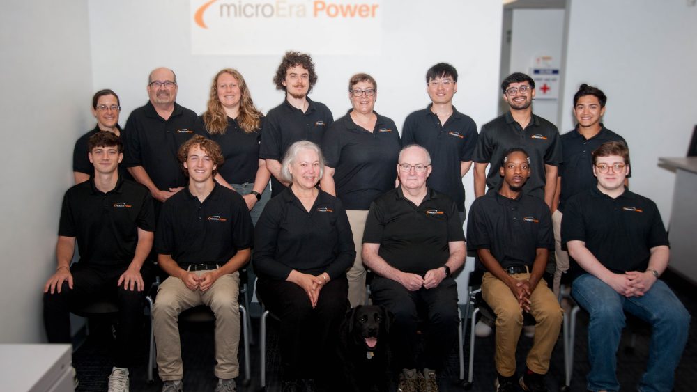 A group of 14 people in black shirts pose and smile for the camera.