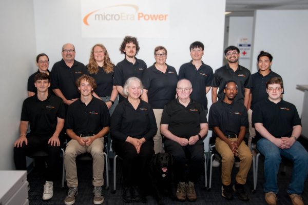 A group of 14 people in black shirts pose and smile for the camera.