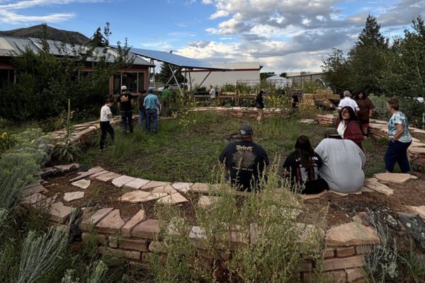 Students sit on a circular rock wall around a garden outside a high school.