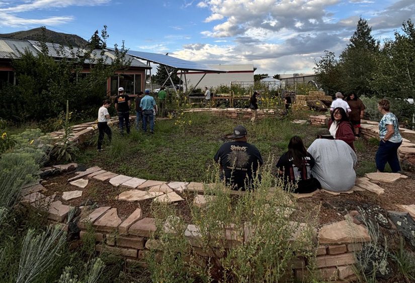 Students sit on a circular rock wall around a garden outside a high school.