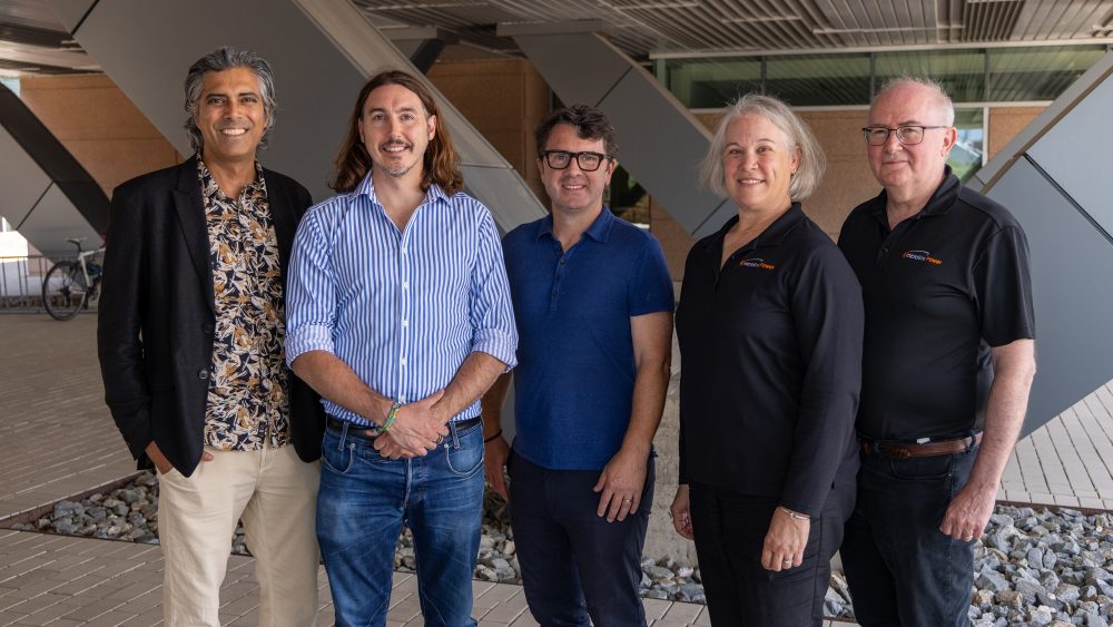 Five people stand outside under a building and smile at the camera.