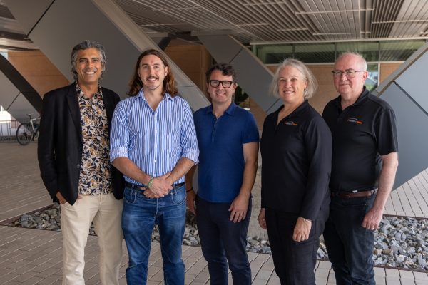 Five people stand outside under a building and smile at the camera.