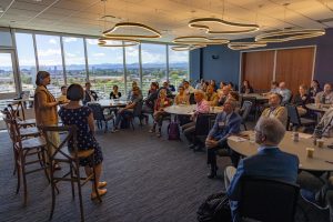 Two people stand in front of a room of tables with people