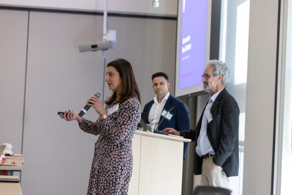 Three people stand around a podium while one speaks into a microphone.