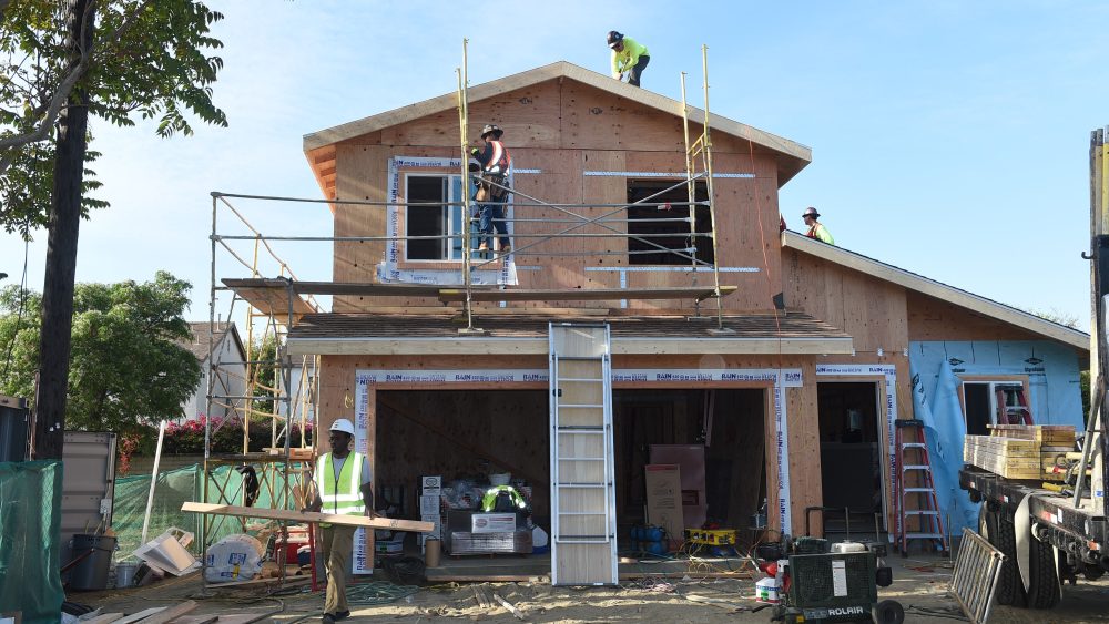 A home under construction with three men in hardhats working on different areas of the home.