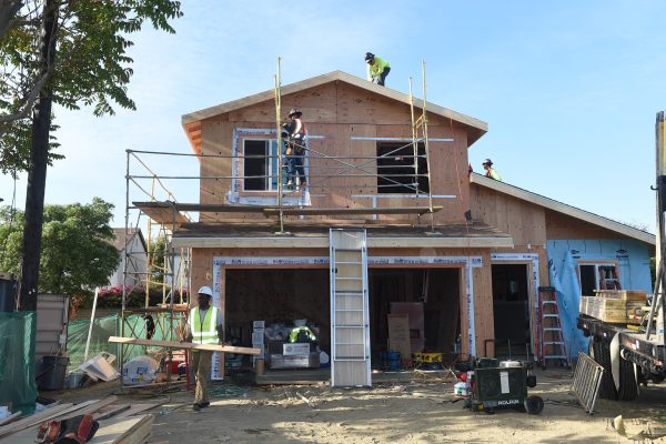A home under construction with three men in hardhats working on different areas of the home.